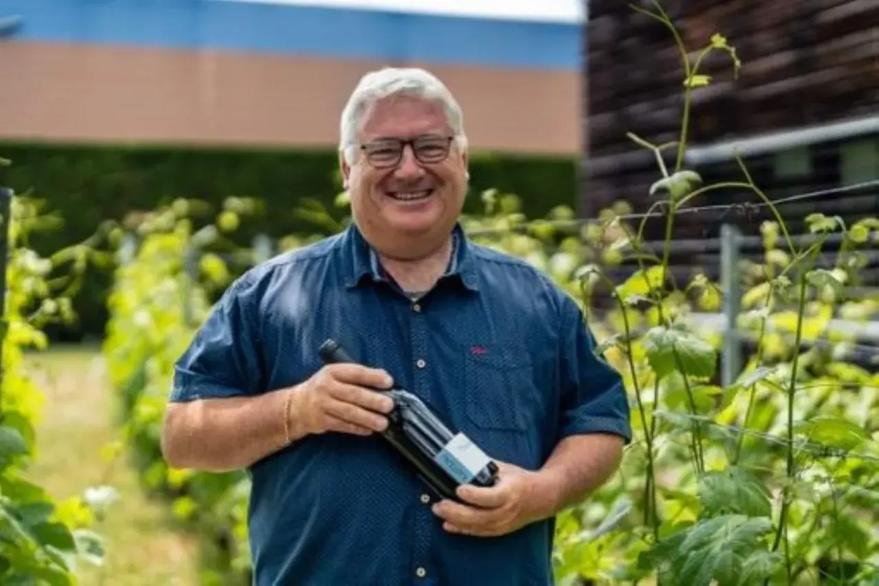 Un vigneron souriant tient une bouteille de vin dans les vignes du domaine du Trapadis.