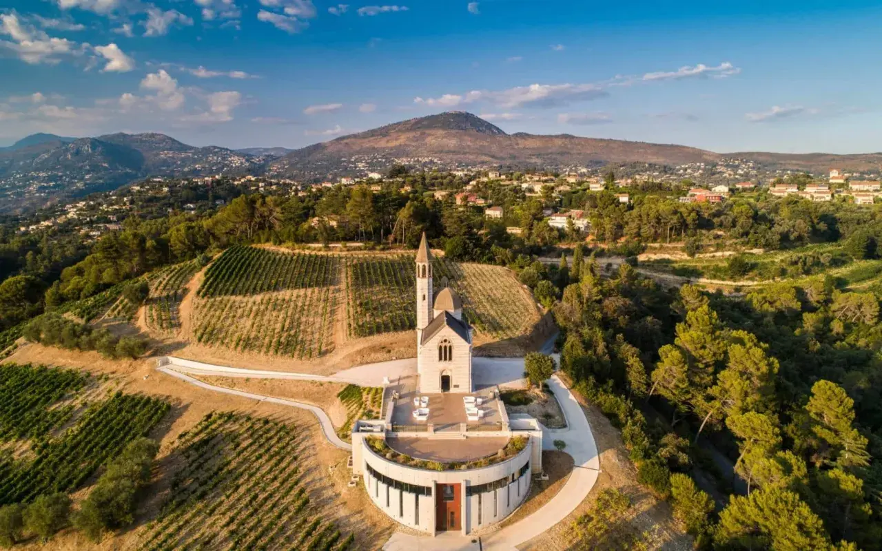 Vue aérienne du **château de Bellet**, avec ses vignobles en terrasses, son église et les collines niçoises en arrière-plan.