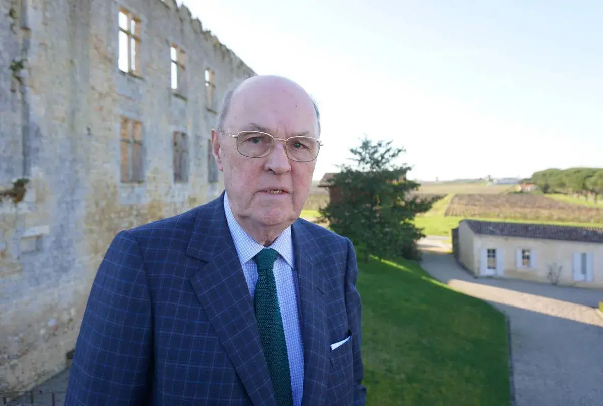 Alexandre de Lur Saluces, un homme d'affaires distingué, pose devant un château historique, les vignobles s'étendant à l'horizon.