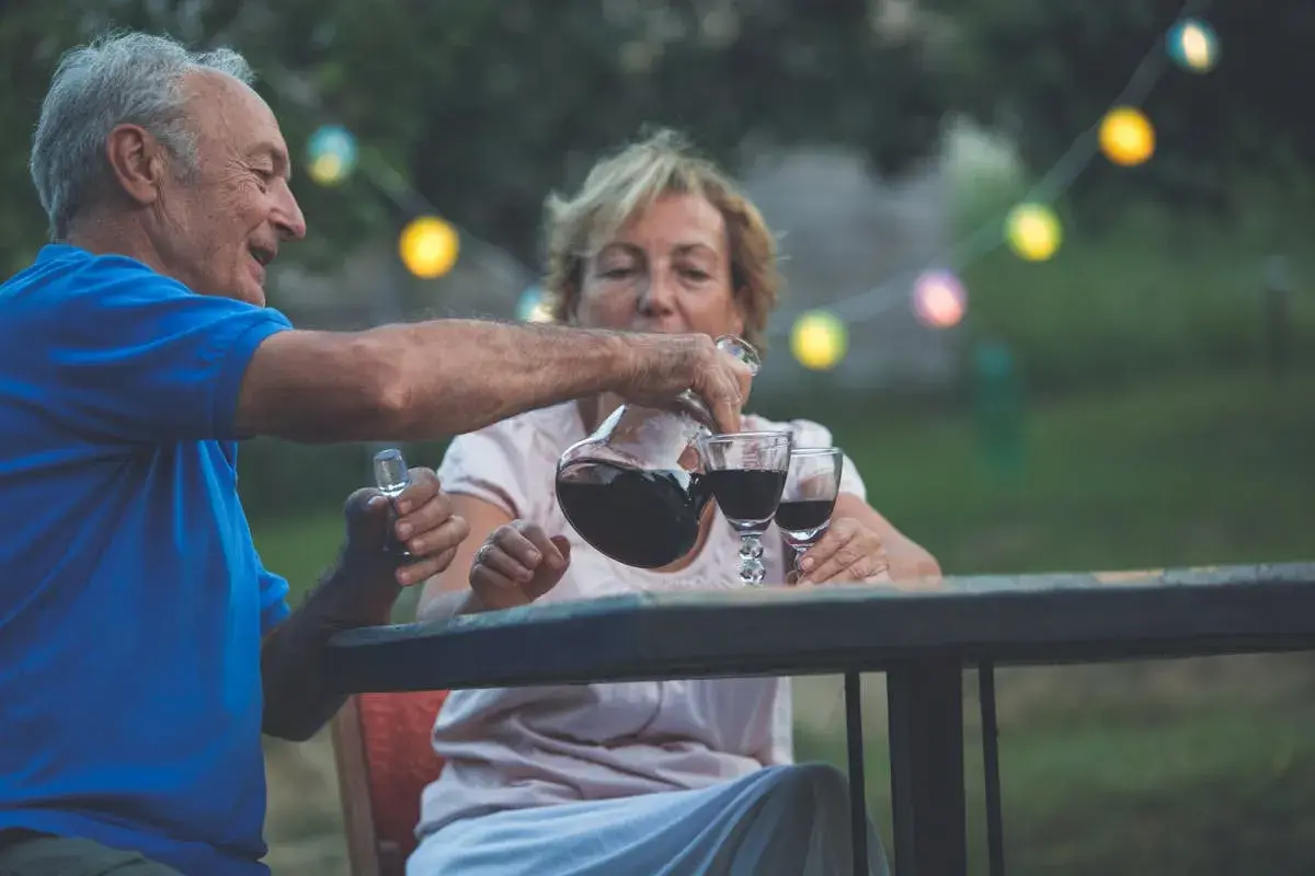 Un couple âgé profite d'un verre de vin par jour dans le jardin, sous des guirlandes lumineuses.