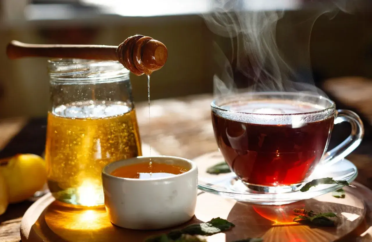 Une boisson eau et miel fumante, avec un pot de miel et une cuillère en bois dégoulinant.
