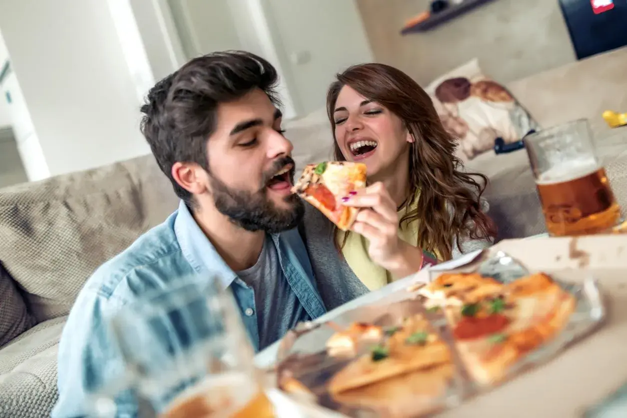 Un couple partage une pizza et de la bière, oubliant le régime pour un moment de plaisir gourmand.