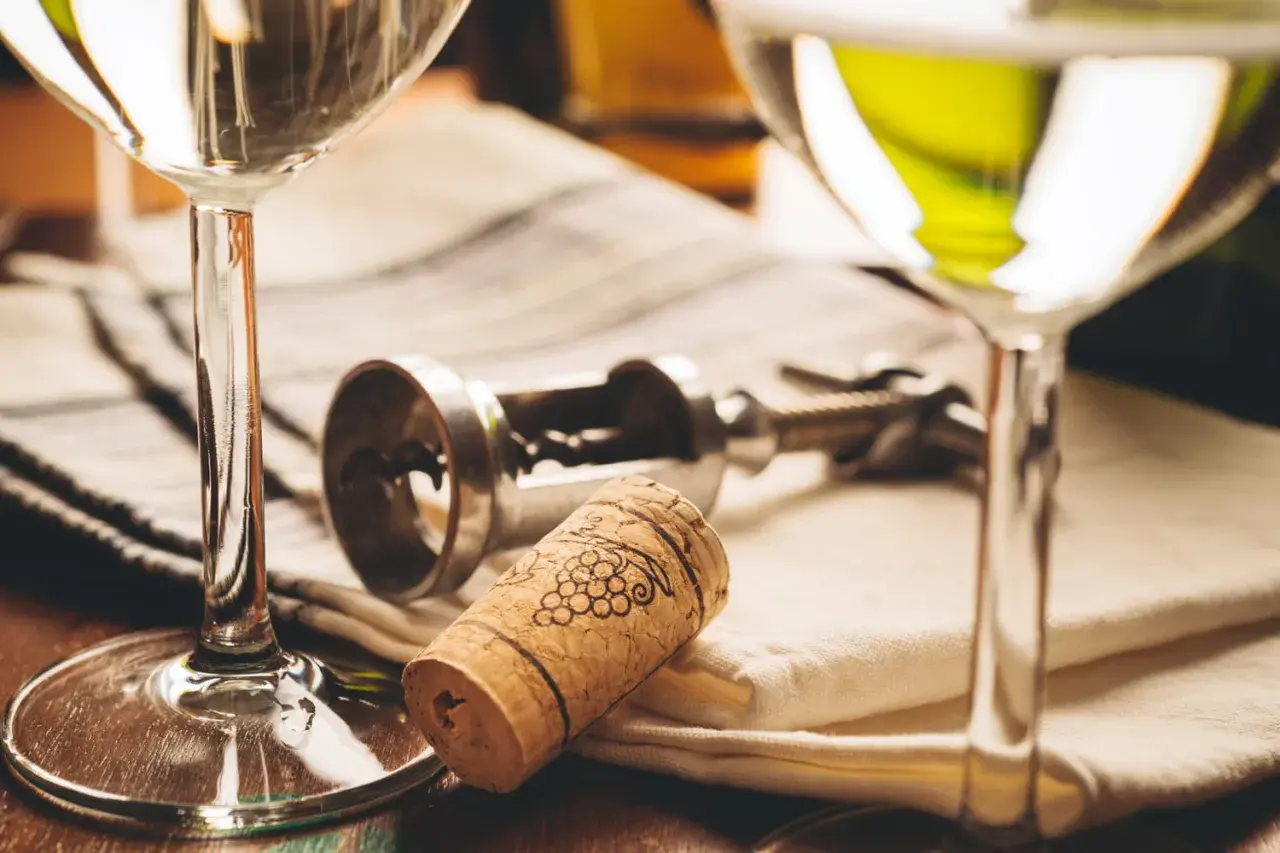 Deux verres de vin blanc, un tire-bouchon et un bouchon orné de grappes de raisin. Le droit de bouchon prix est souvent discuté lors de dégustations.