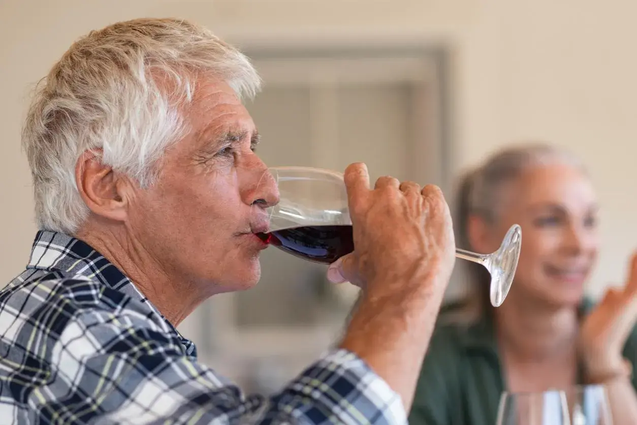 Un homme âgé boit du vin rouge. Attention, le vin périmé présente un danger.