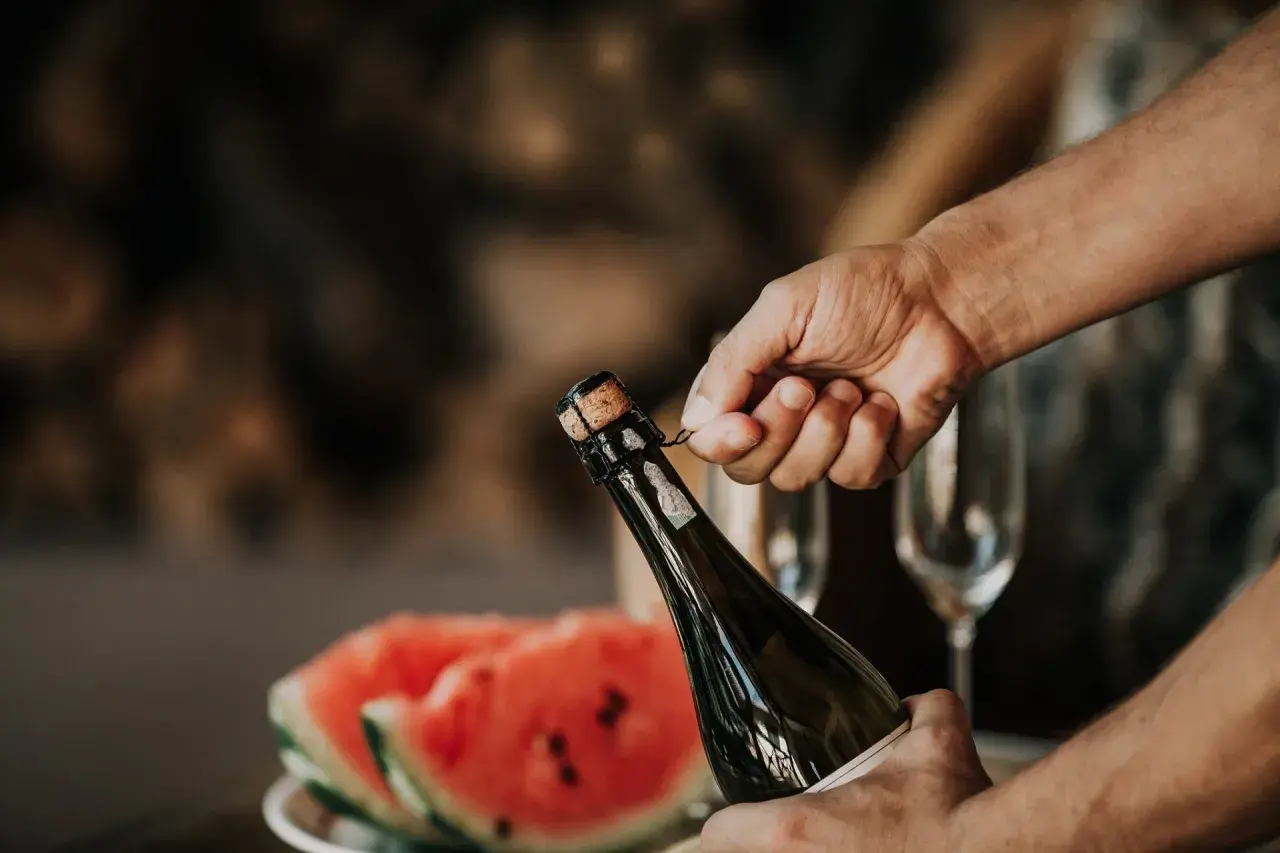Main tenant du goulot, une main dépose délicatement le muselet. La clé pour savoir comment ouvrir une bouteille de champagne est dans ce geste précis.