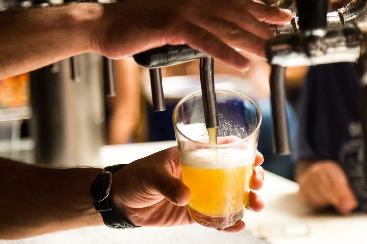 Main d'un homme servant une bière blonde dans un verre. Une question se pose : pourquoi la bière donne envie de faire pipi ?