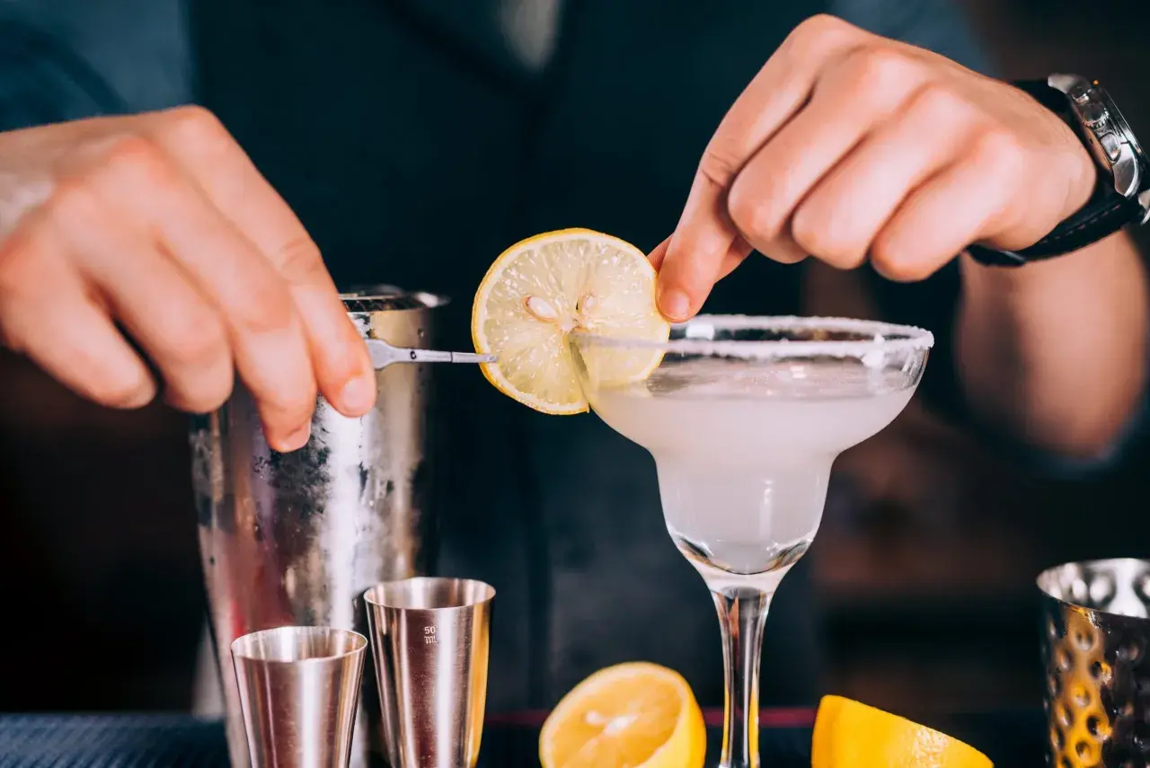 Un barman prépare un cocktail en p. avec une tranche de citron.