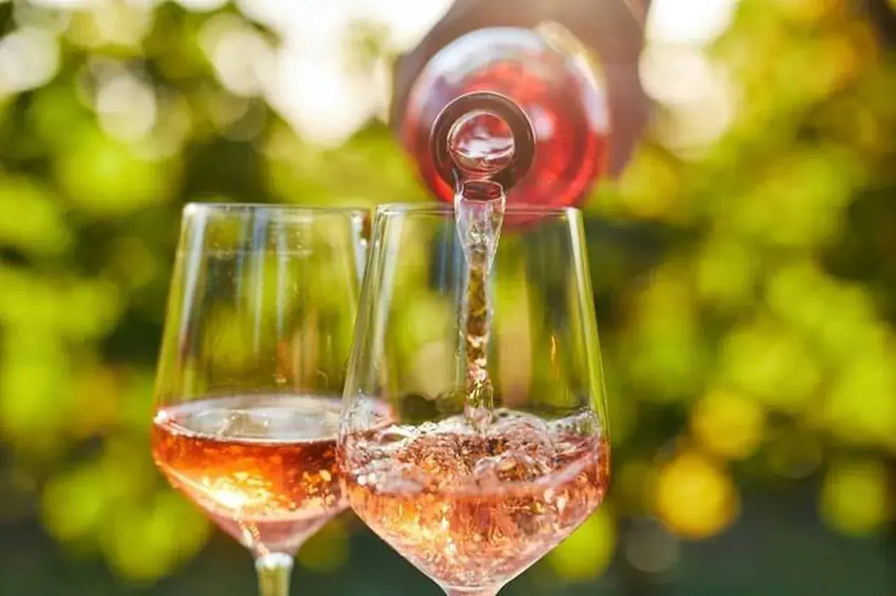 Un verre de rosé est servi dans un autre verre, sous un soleil radieux. Un moment parfait pour boire du rosé tous les jours.