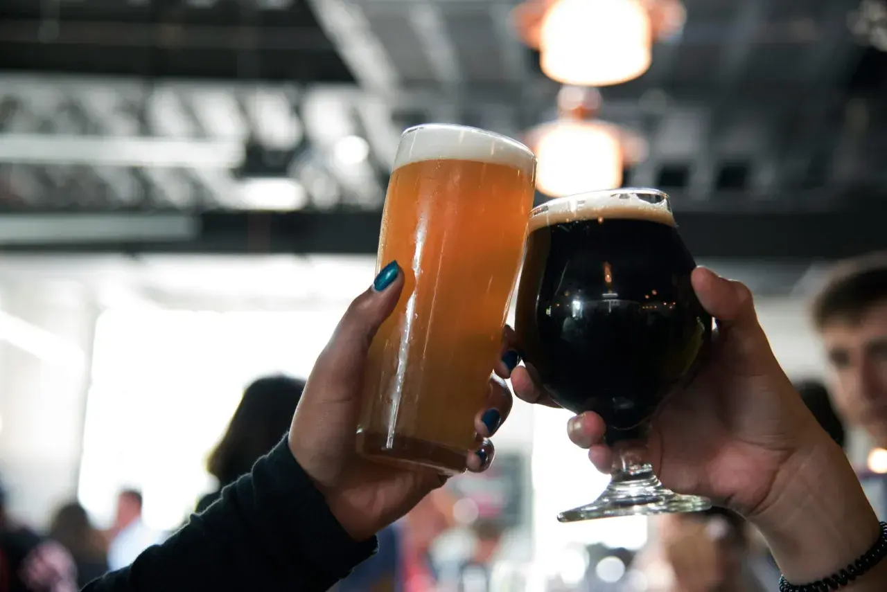 Deux mains lèvent des verres de bière, l'un blond et l'autre brun, pour un toast.