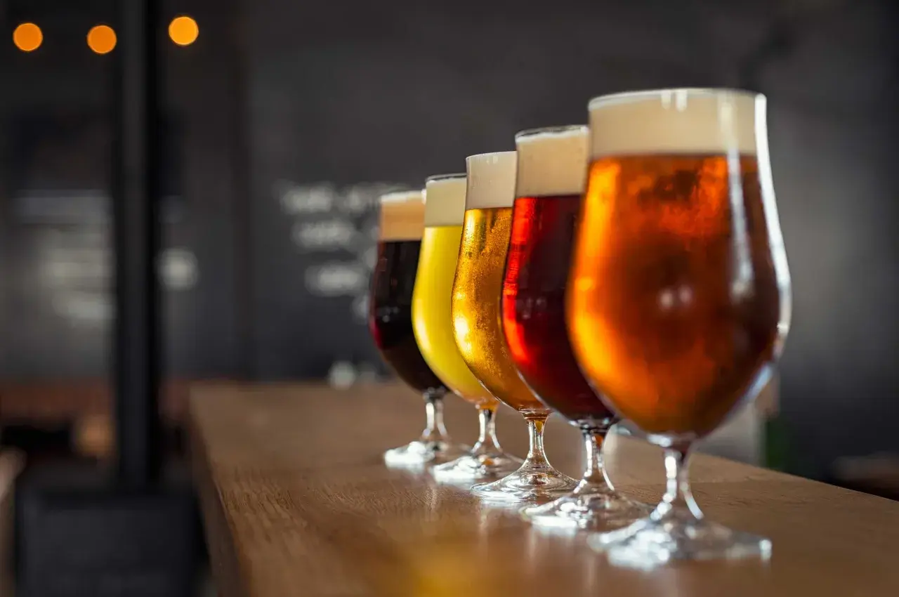 Une dégustation de différents types de bière, alignés sur un comptoir en bois. Les verres présentent des couleurs allant du blond doré au brun foncé, avec une mousse crémeuse.
