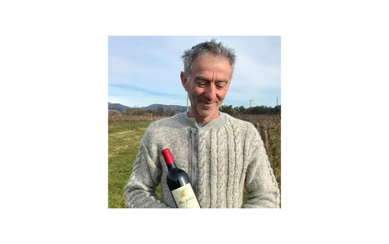 Un homme souriant tient une bouteille de vin Mas Jullien dans un vignoble.
