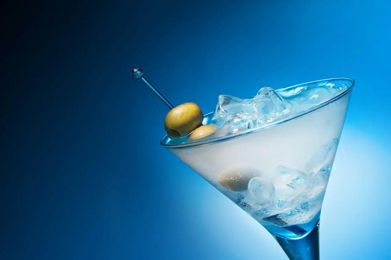 Un cocktail gin martini glacé, avec des olives sur un cure-dent bleu, sur fond bleu dégradé.