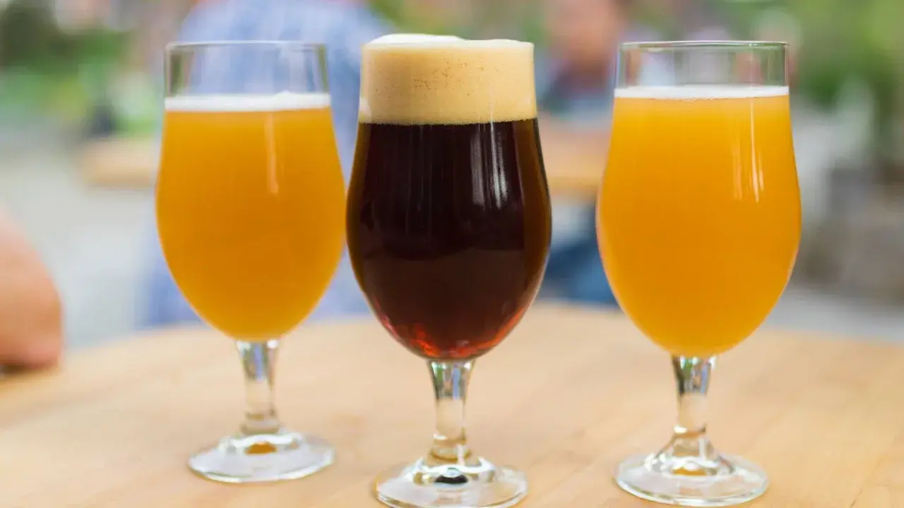 Trois verres de bière, deux blondes et une brune, sur une table en bois. Une dégustation pour comparer le goût et le calorie biere.