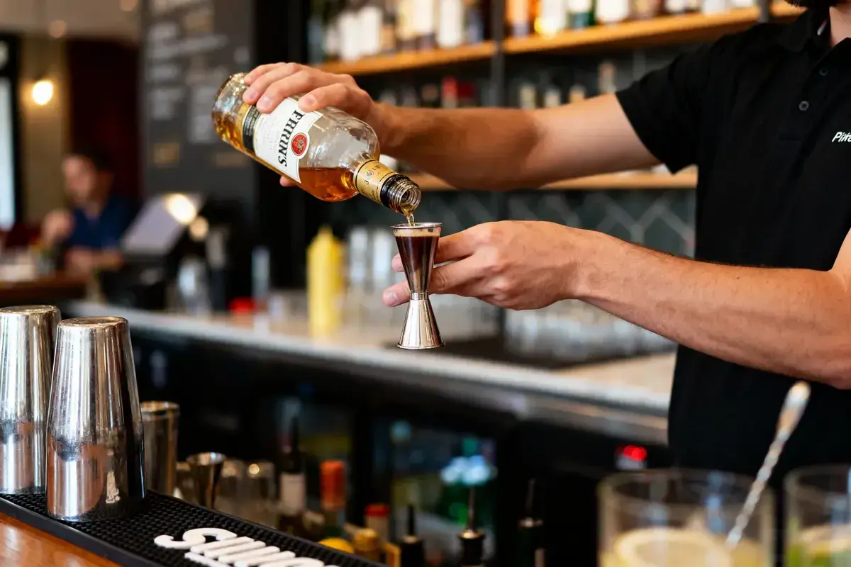 Un barman verse du whisky d'une bouteille dans un doseur. Il prépare un cocktail, prêt à boire à la bouteille ou au verre.