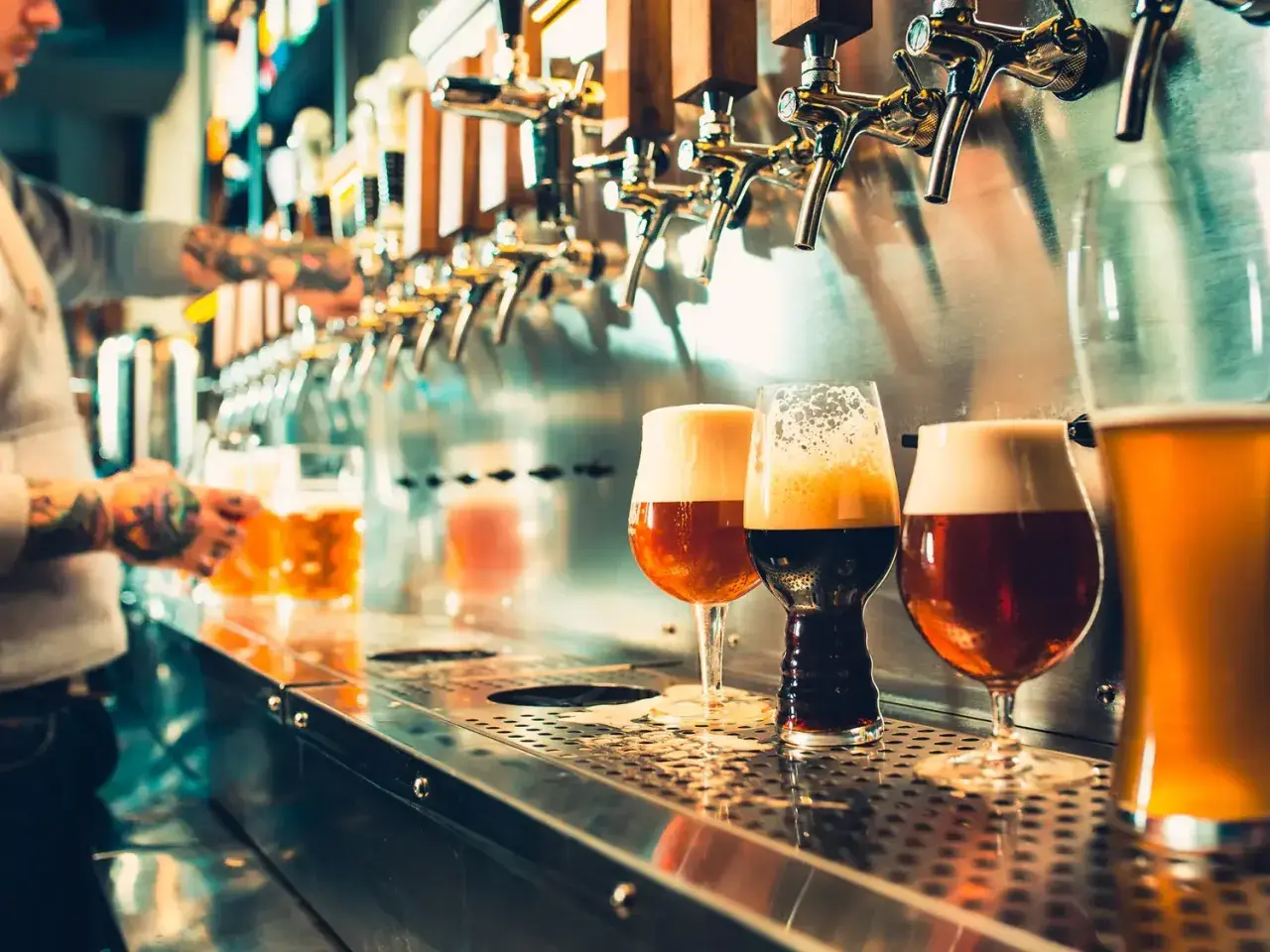 Verre de bière au bar, avec un barman en arrière-plan qui sert une chope.