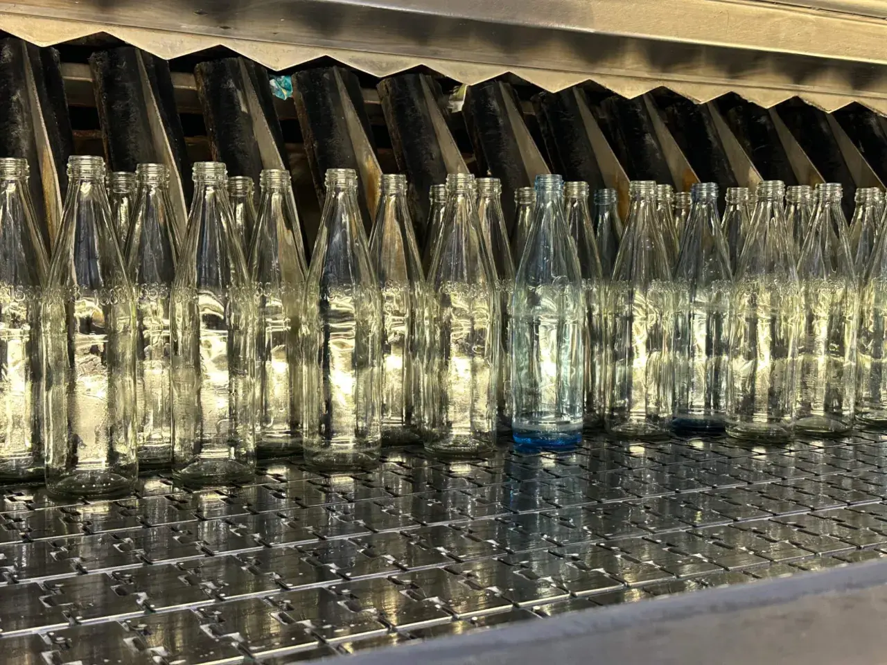 Une rangée de bouteilles en verre transparentes alignées sur une chaîne de production. On se demande combien de verre dans une bouteille d'eau.
