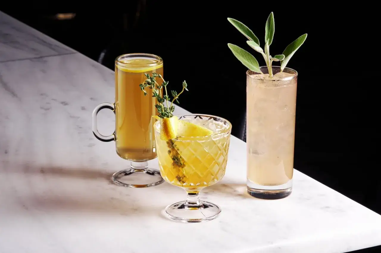 Trois cocktails rafra&icirc;chissants, dont un avec du thym et du citron, sont pr&eacute;sent&eacute;s sur un comptoir en marbre.