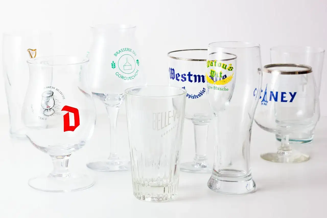 Collection de verres à bière belge, chacun portant le nom d'une brasserie renommée.