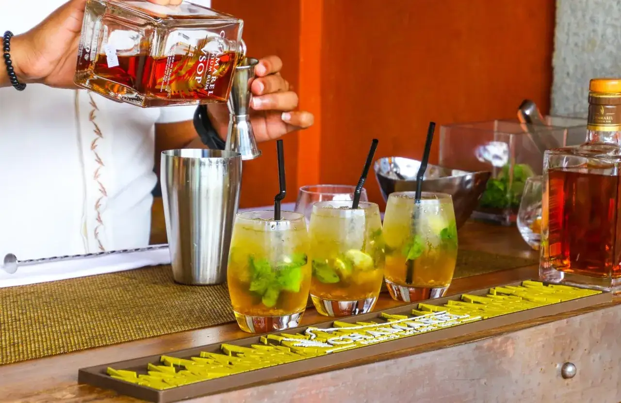 Un barman prépare un cocktail en p. Trois verres remplis de glaçons, menthe et citron vert attendent d'être servis.