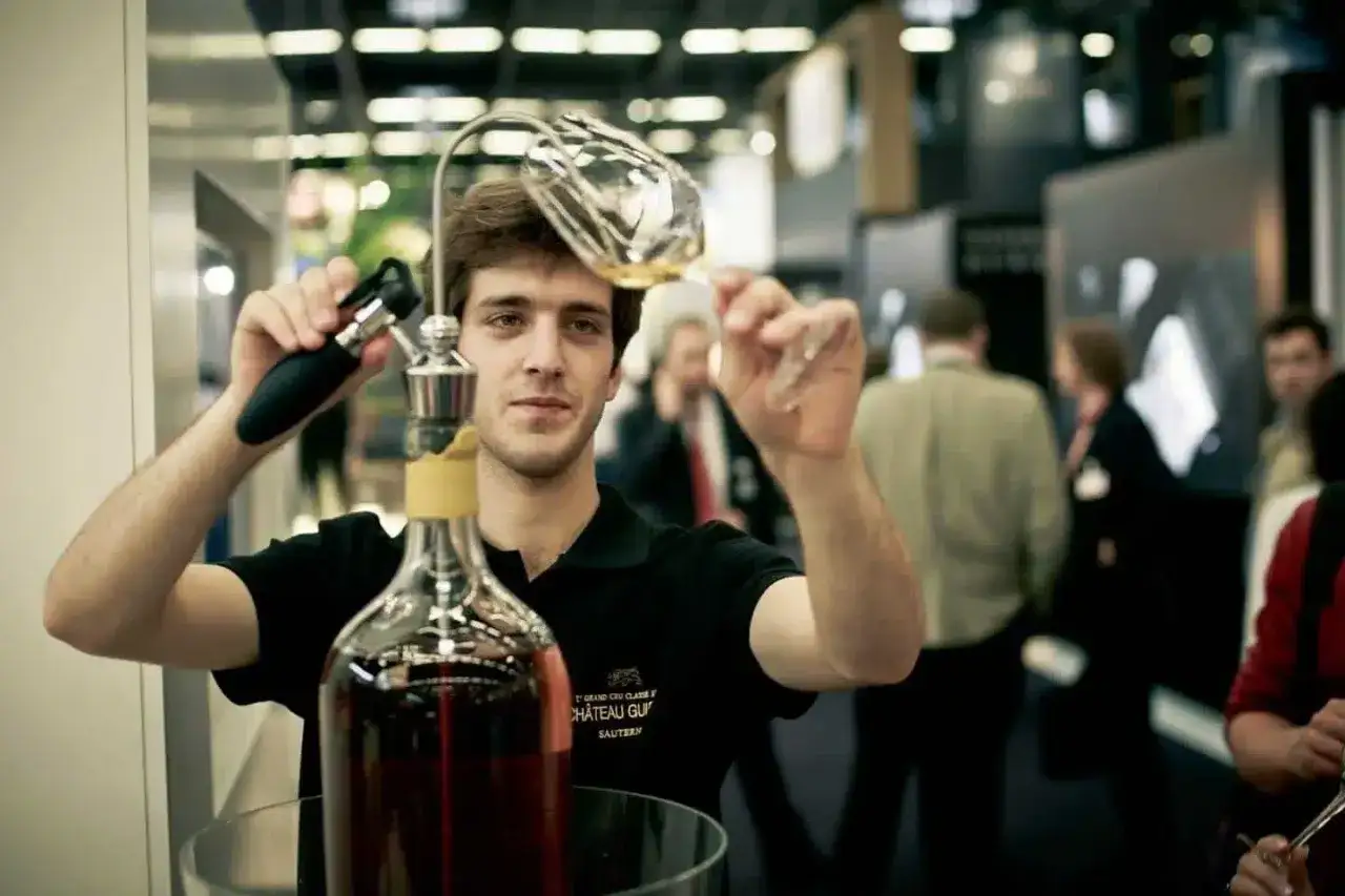 Un homme sert du vin d'une tr&egrave;s grande bouteille, peut-&ecirc;tre la plus grande bouteille du monde, dans un verre.