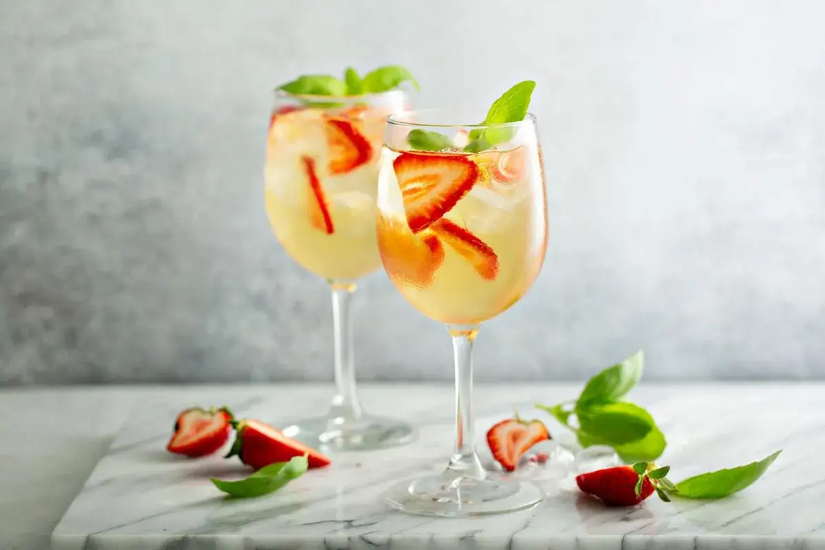 Deux verres de cocktail vin blanc vodka, garnis de fraises et de basilic, sur un fond gris.