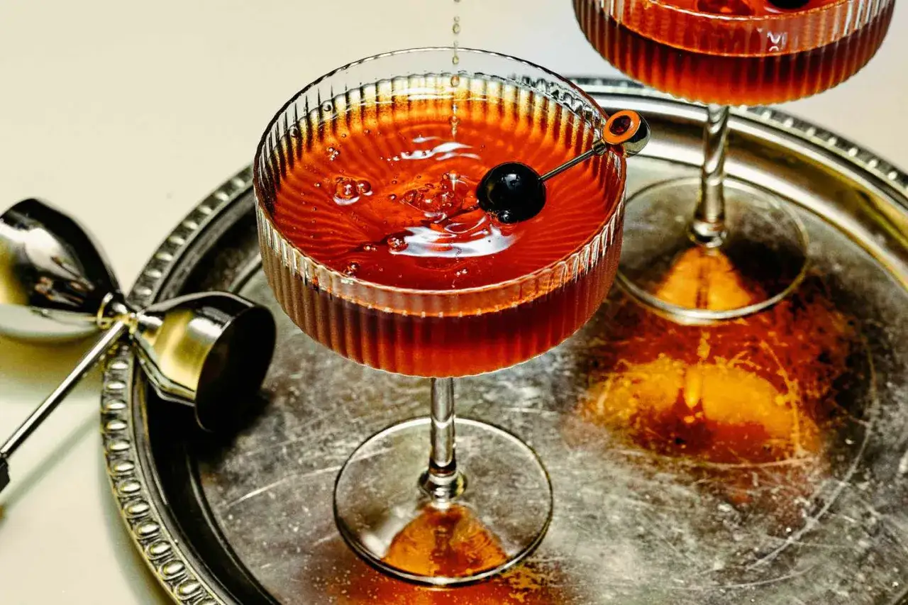 Un cocktail vermouth ambré, garni d'une cerise noire, sur un plateau argenté avec un jigger.