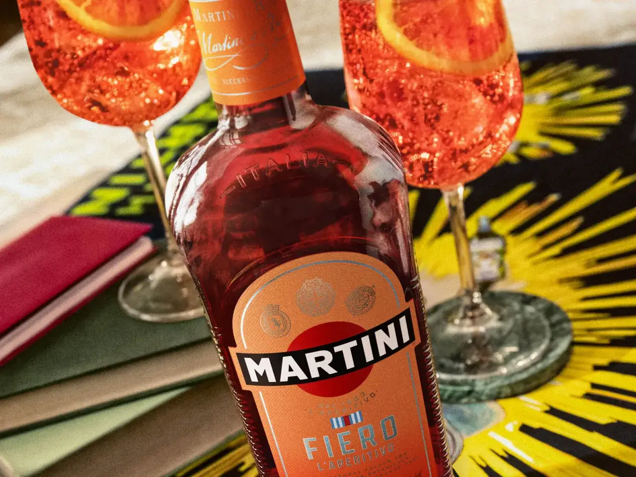 Bouteille de Martini Fiero et deux cocktails p&eacute;tillants orn&eacute;s de tranches d'orange, pr&ecirc;ts pour un ap&eacute;ritif.