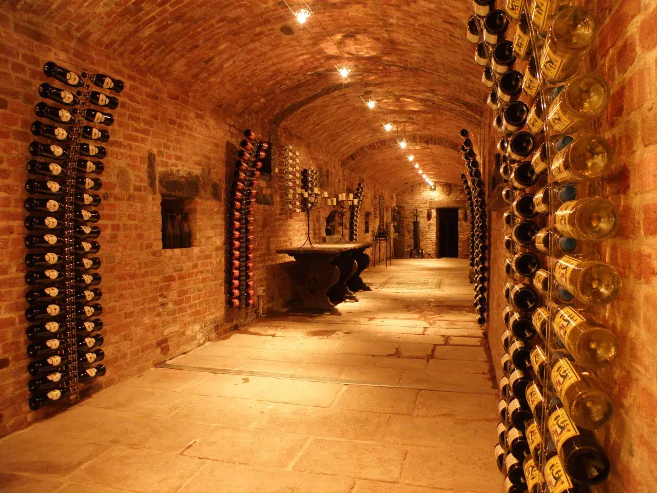 Cave à vin en briques avec des bouteilles de vin rangées sur des étagères murales. On y voit comment conserver le vin debout ou couché.
