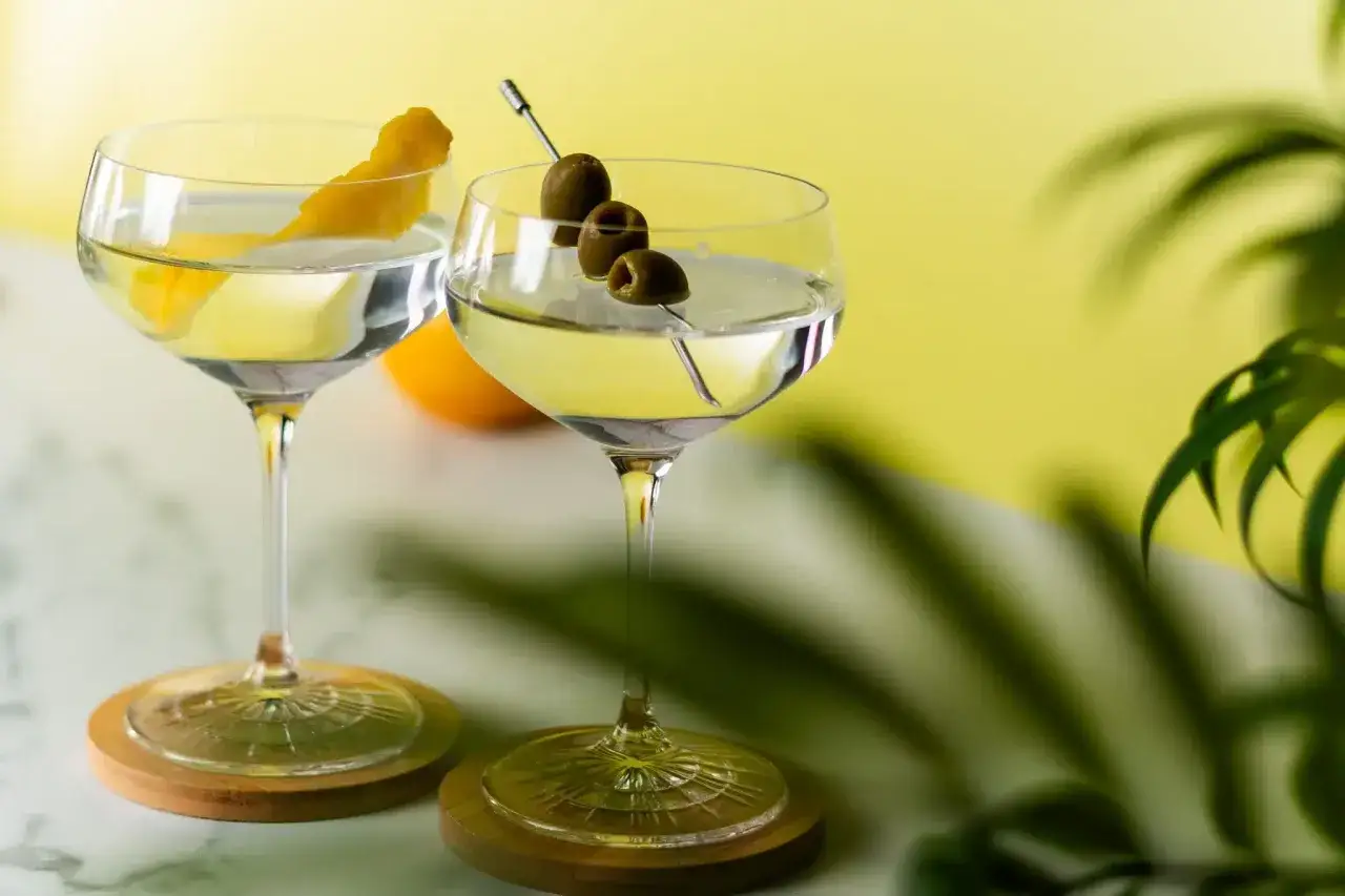 Deux verres de dry martini cocktail, l'un garni d'un zeste de citron, l'autre de trois olives sur une pique.