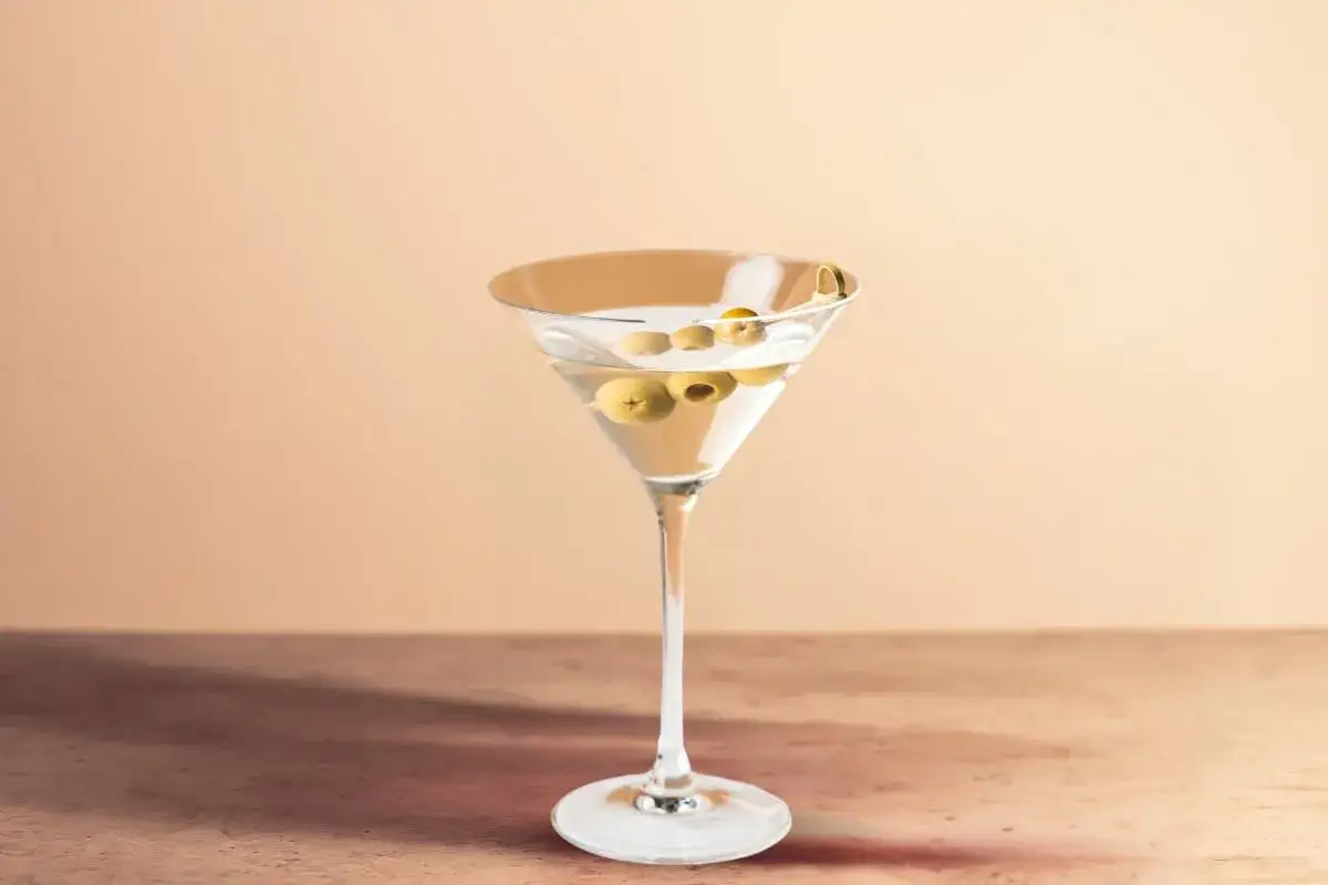 Un verre de martini vodka, garni d'olives, sur un fond pastel.