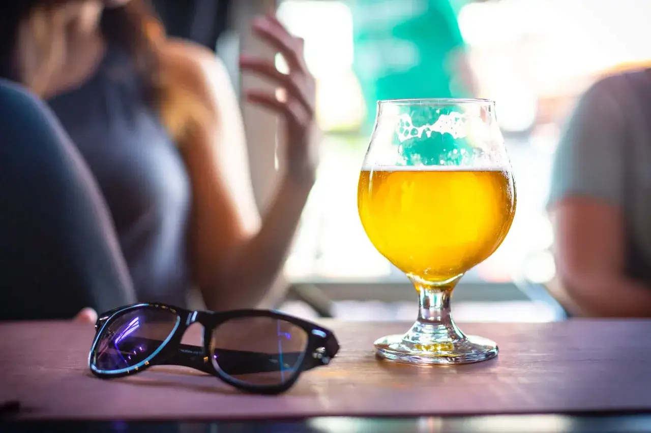 Un verre de bi&egrave;re de printemps dor&eacute;, mousseux, sur une table en bois, avec des lunettes de soleil &agrave; c&ocirc;t&eacute;.