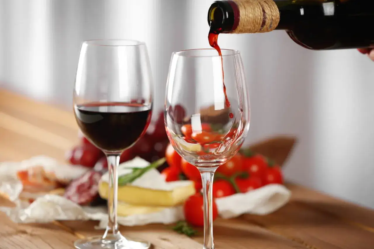 Un verre de vin rouge est servi, &agrave; c&ocirc;t&eacute; d'un autre d&eacute;j&agrave; rempli. Des grappes de raisin, des tomates et du fromage compl&egrave;tent cette sc&egrave;ne gourmande de vin au verre.