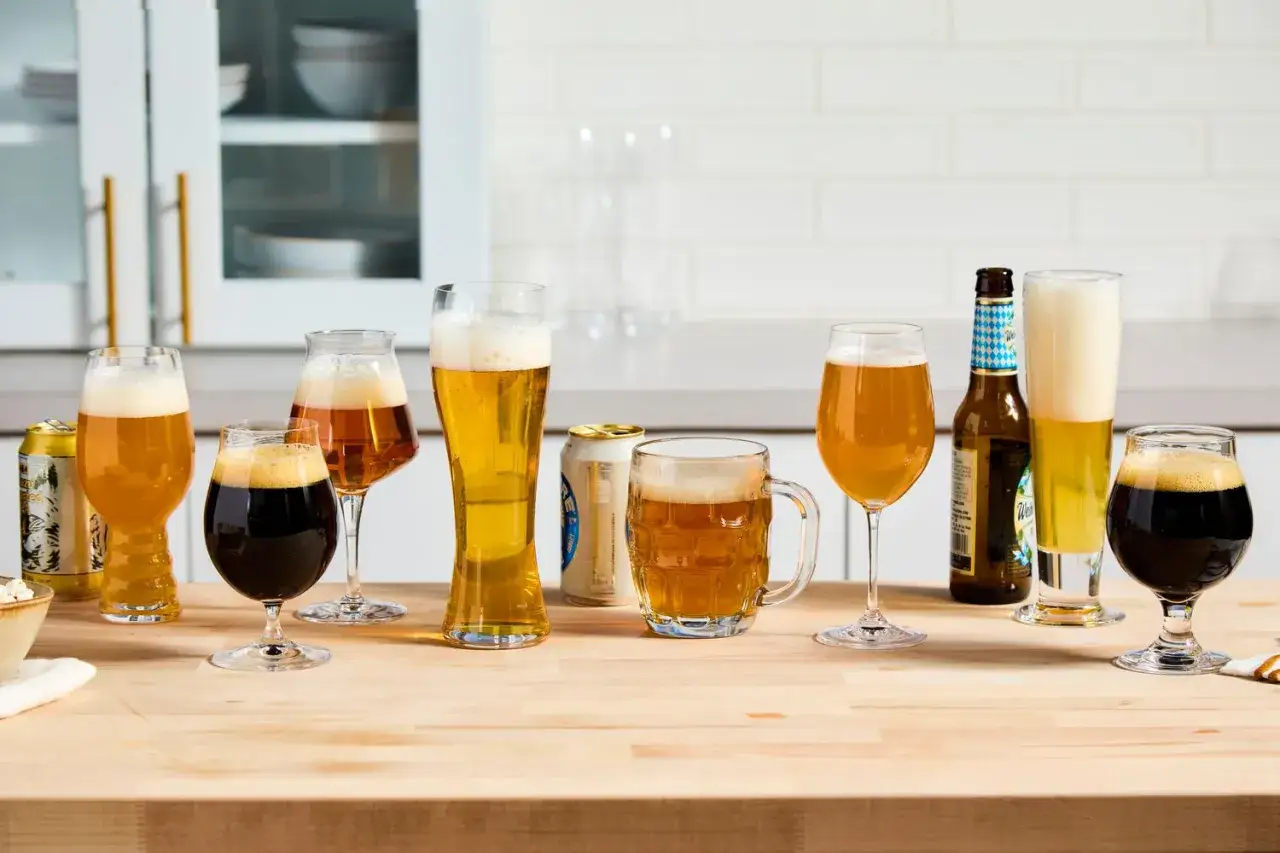 Diverses bières, dont une pinte, dans des verres variés et des canettes, sur un comptoir en bois.