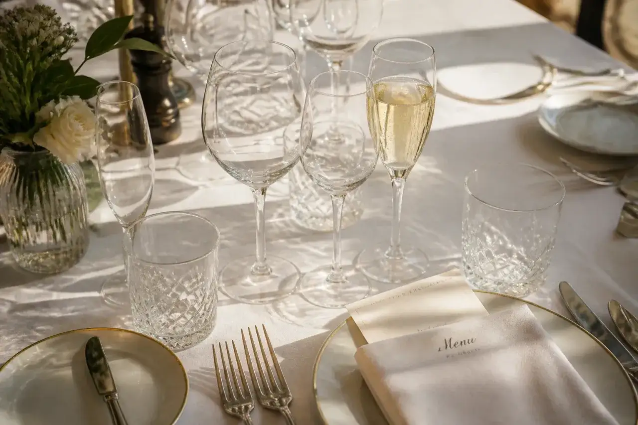 Une table dress&eacute;e pour un repas, avec des verres de diff&eacute;rentes formes, un menu et des couverts. Une histoire du verre &agrave; travers ces objets &eacute;l&eacute;gants.
