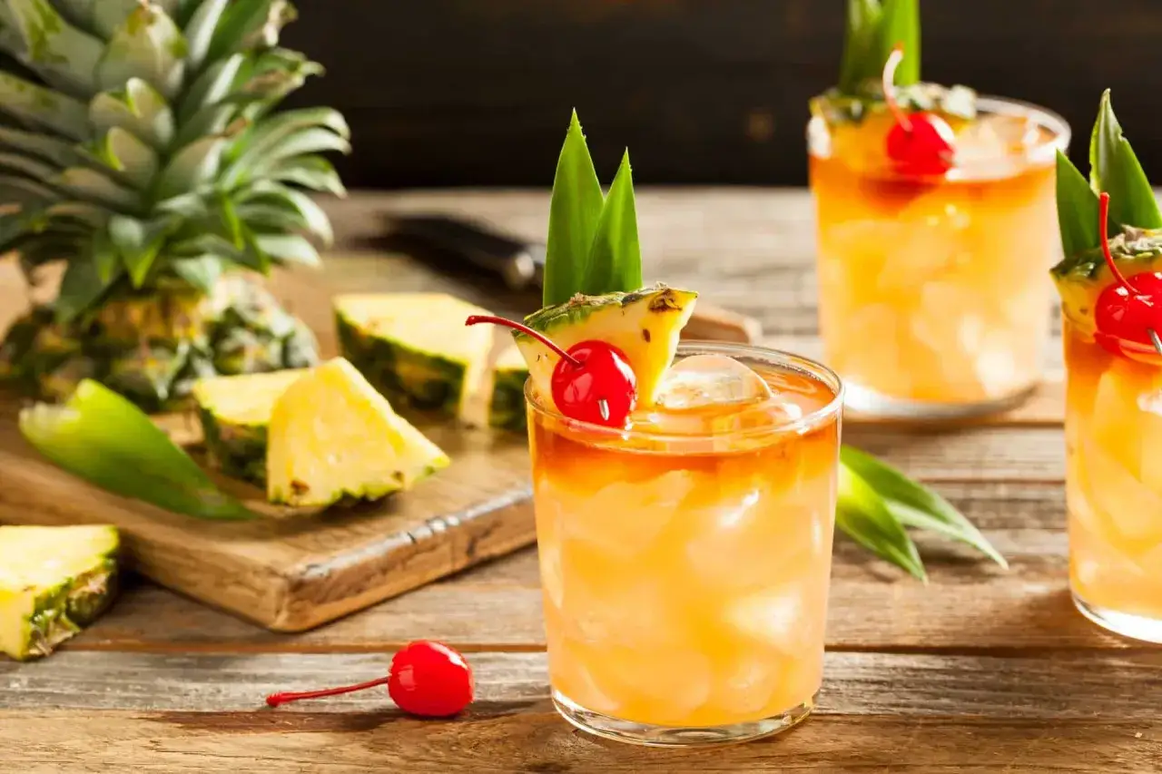 Cocktail rhum fraise ananas, garni d'une cerise et d'une feuille d'ananas, sur fond de fruits frais.