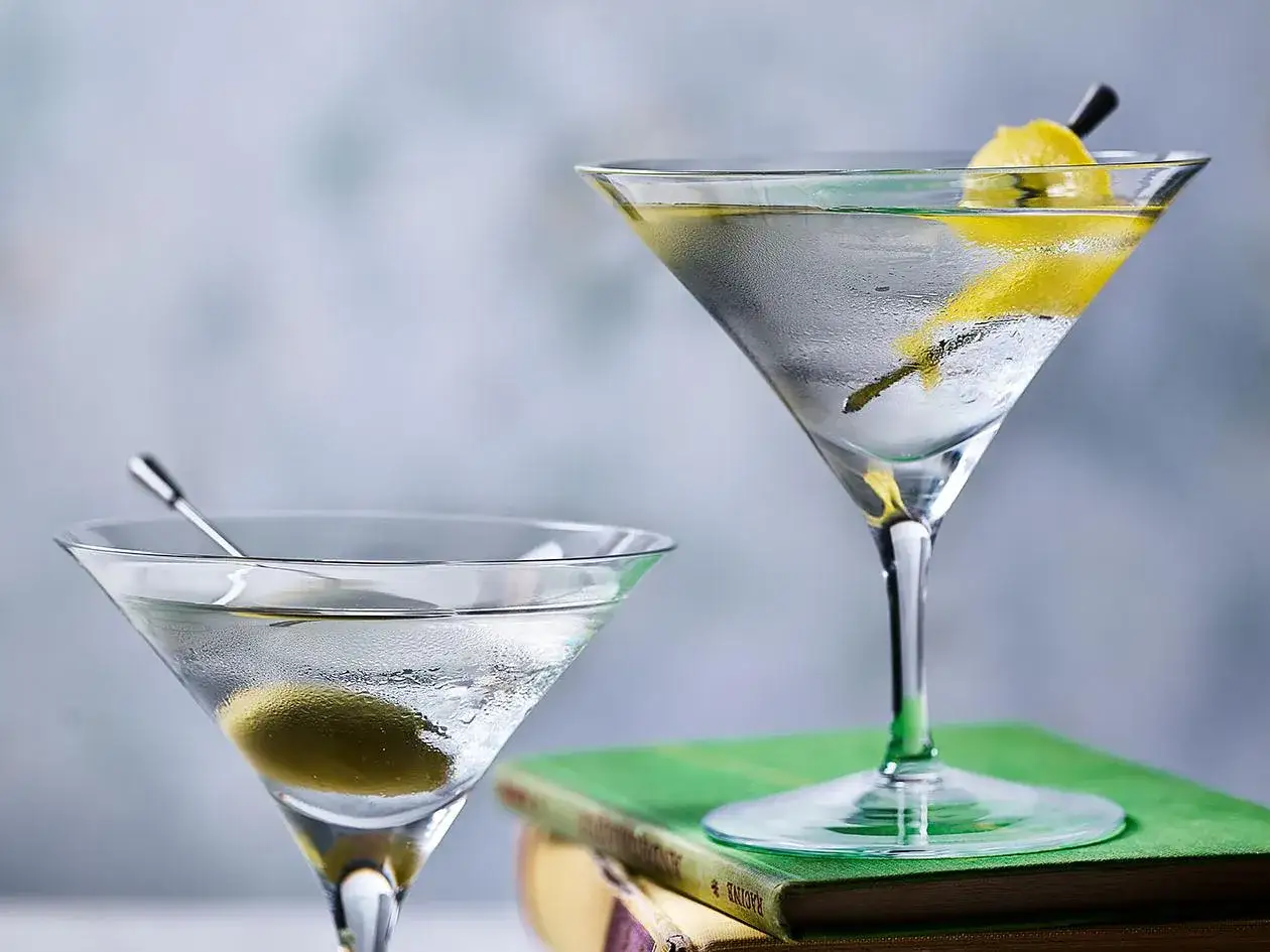 Deux verres de cocktail martini, l'un avec une olive, l'autre avec un zeste de citron, pos&eacute;s sur des livres.