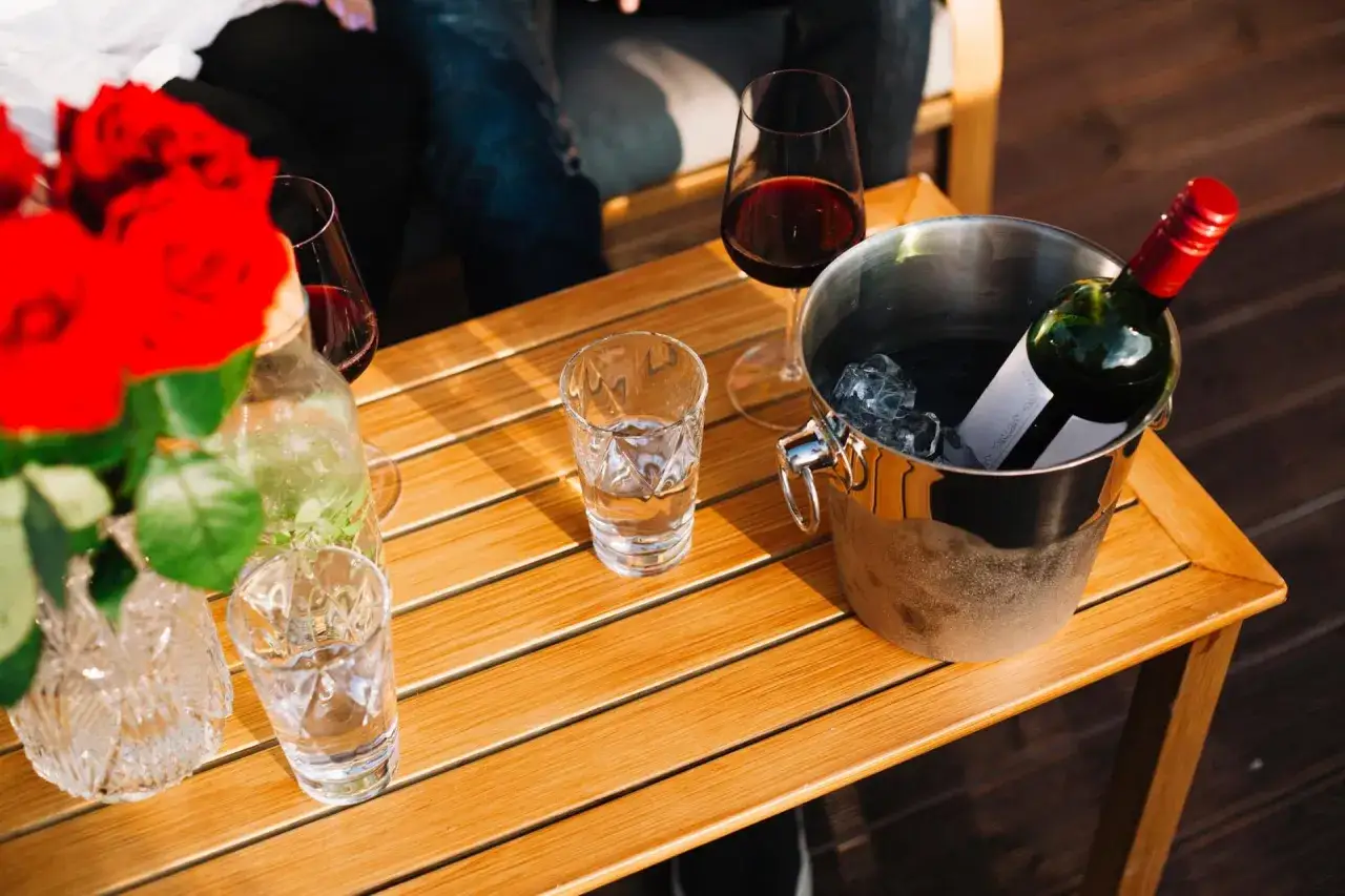 Seau &agrave; glace pour garder le vin au frais &agrave; table, avec des verres et des roses rouges.