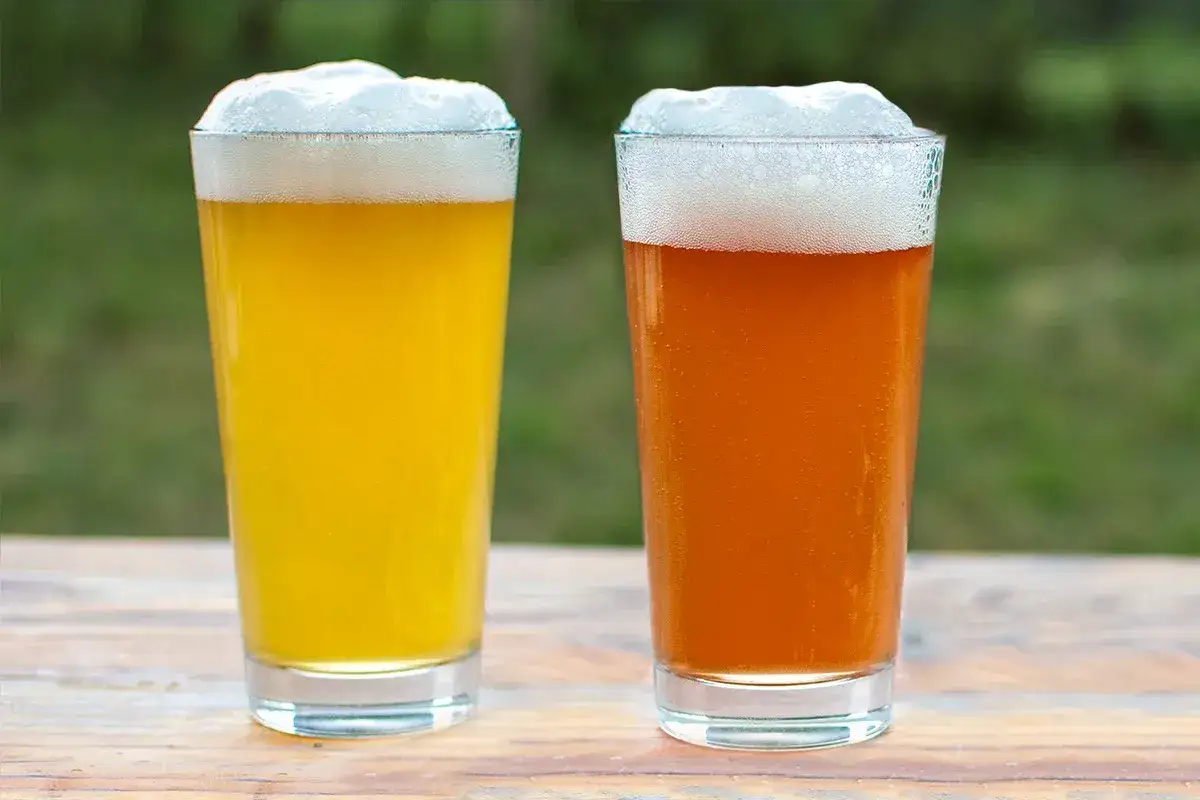 Deux verres de bi&egrave;re, l'un jaune p&acirc;le, l'autre ambr&eacute;, sur une table en bois. Une pale ale ou une IPA pour se rafra&icirc;chir.
