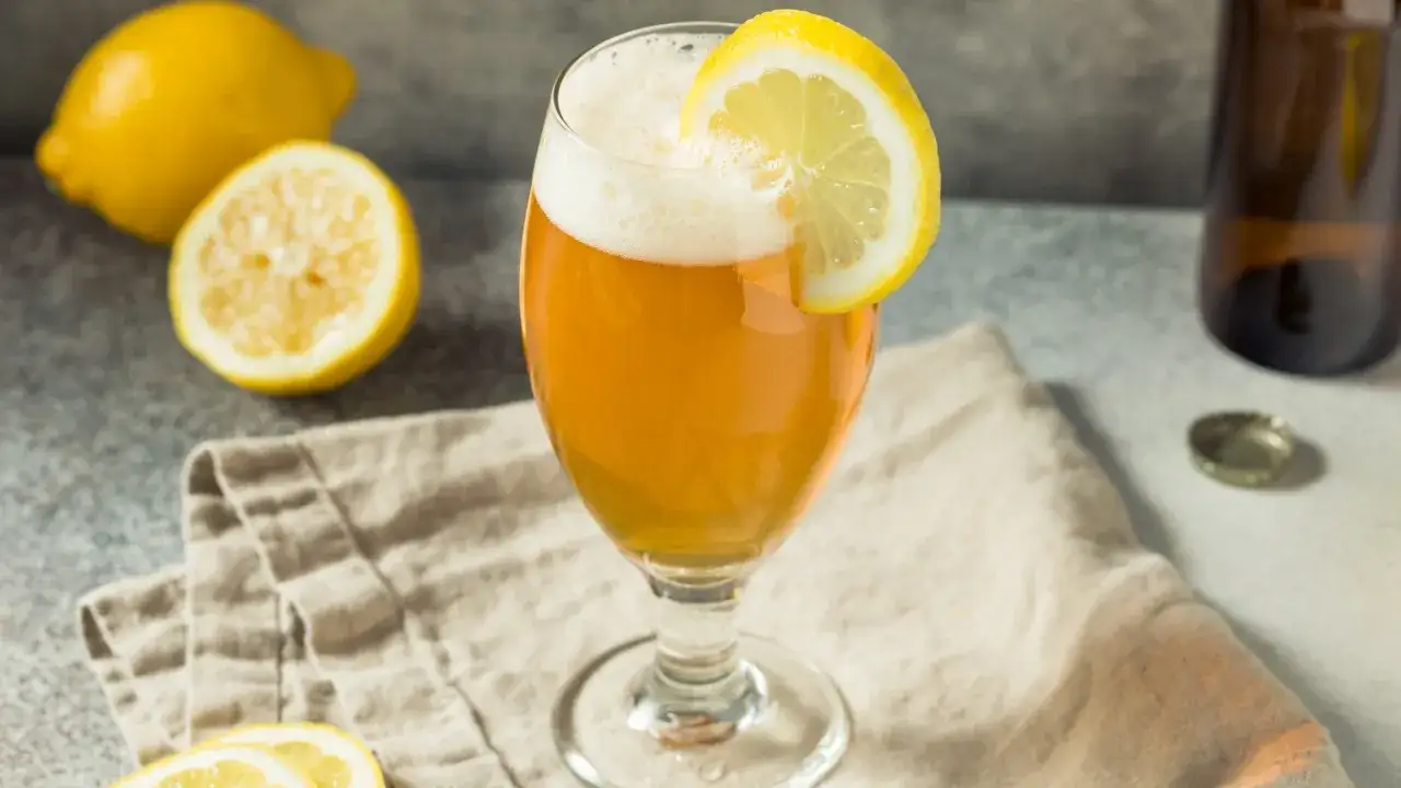 Verre de bi&egrave;re ambr&eacute;e avec une tranche de citron, accompagn&eacute; de citrons frais et d'une bouteille. Un nom de bi&egrave;re citron parfait pour l'&eacute;t&eacute;.