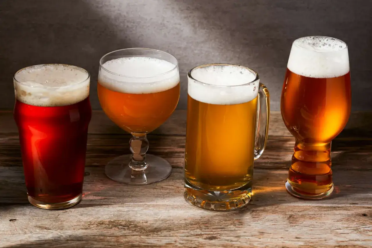 Quatre verres de bi&egrave;re aux couleurs vari&eacute;es, du rouge ambr&eacute; au dor&eacute; clair, sur une table en bois rustique.