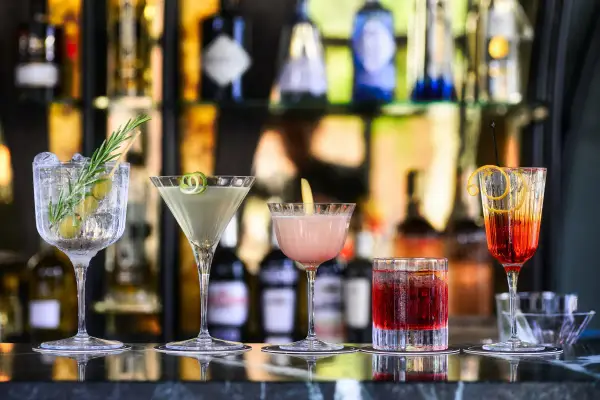 Cinq cocktails colorés, parfaits comme boisson pour ouvrir l'appétit, sont alignés sur un bar.
