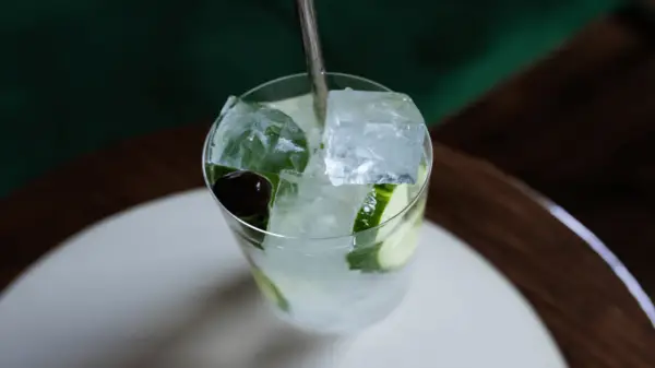 Un verre rempli de glaçons transparents, de rondelles de concombre et d'une cerise, prêt à être dégusté.